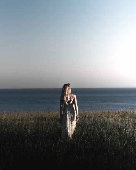 woman wearing a printed long dress walking on grass field near the sea